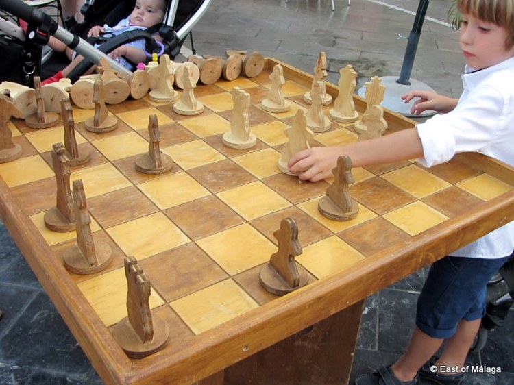Child plays on wooden chess table at medieval market in Torrox pueblo